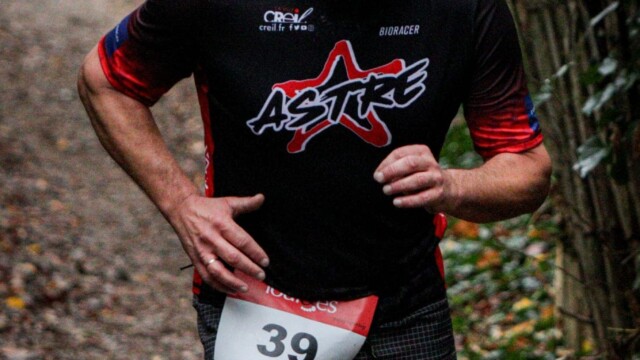 Participant au triathlon à Creil, en pleine course sur un parcours nature forestier. Athlète en course de triathlon enduro avec casque et maillot Astre Creillois.