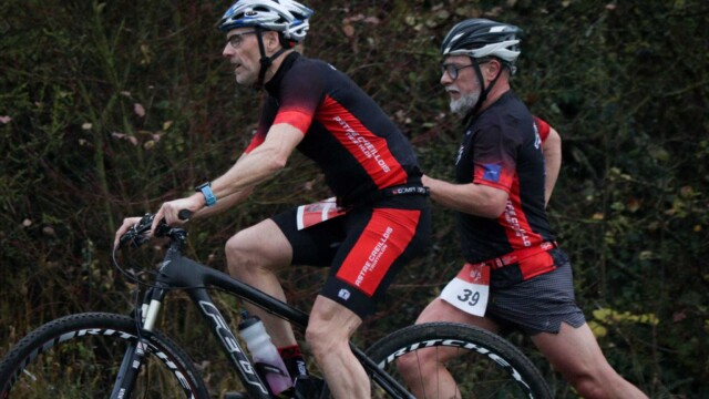 Participants du triathlon Astre Creillois en plein effort de course à vélo dans un décor naturel, démontrant endurance et esprit sportif. Vignette de deux coureurs à vélo lors d'une course de triathlon à Creil, dans un environnement naturel et boisé.